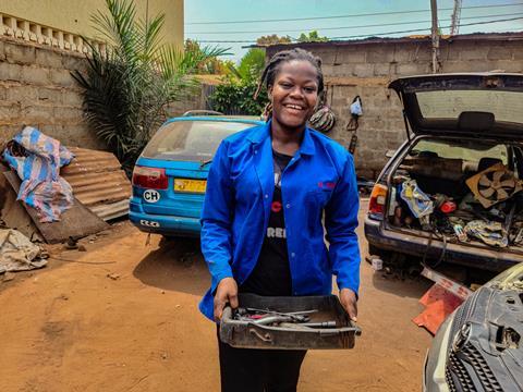 Winner carrying a tray full of tools she is using to repair a car 